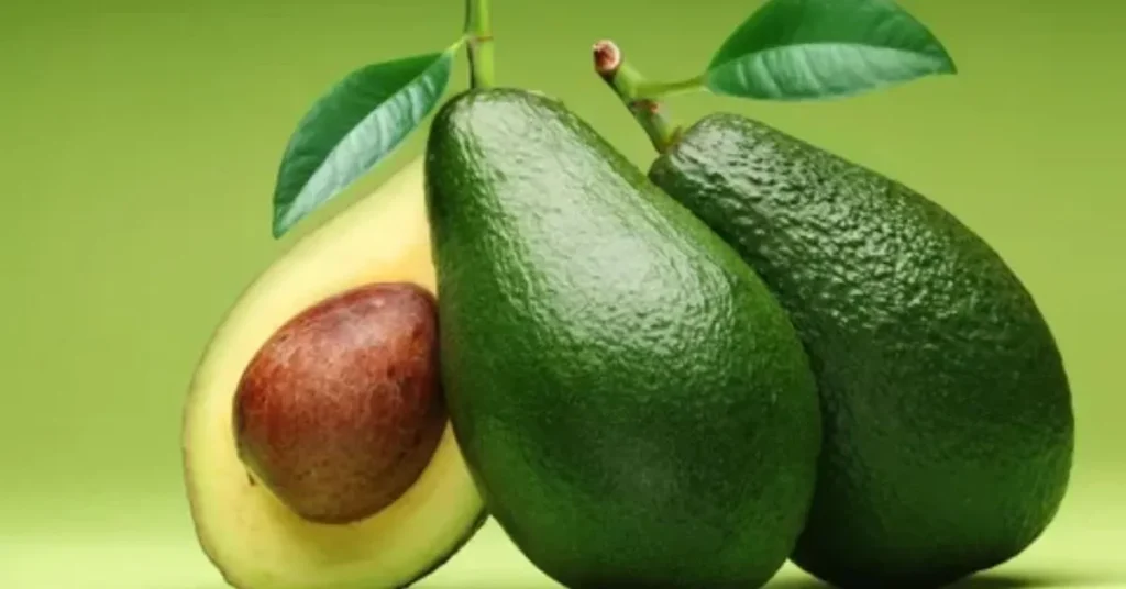 Three ripe avocados, one cut open to reveal its creamy, green flesh and brown pit, against a vibrant green background.