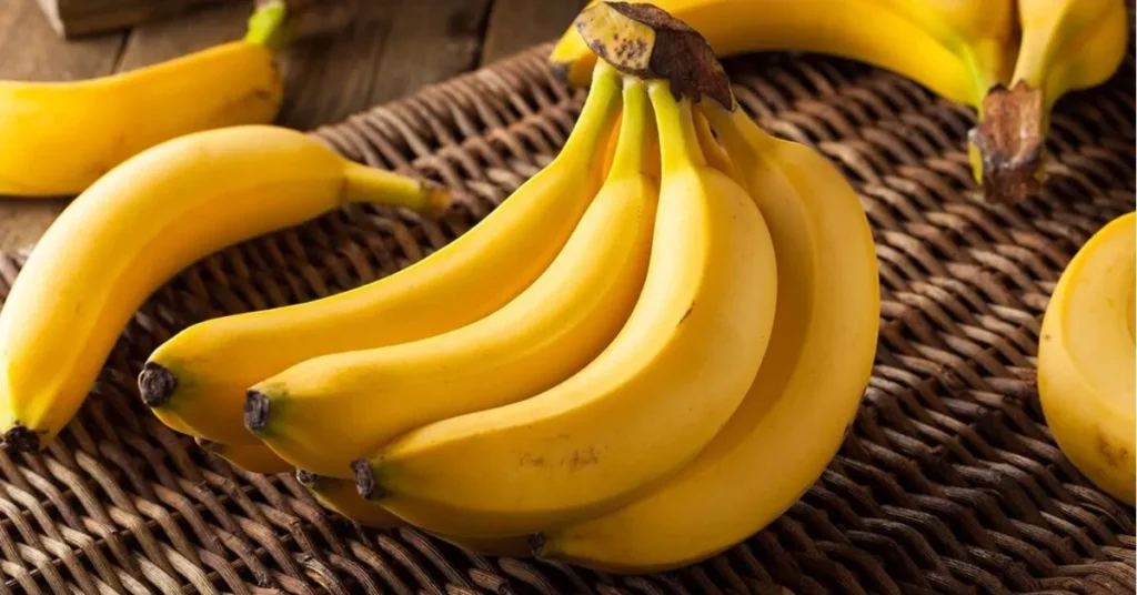 A cluster of ripe yellow bananas resting on a woven mat, with a few scattered bananas nearby, showcasing their fresh and vibrant appearance.