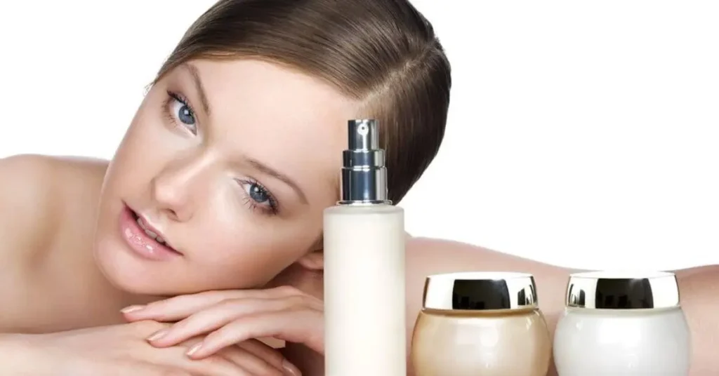 The photograph displays a woman showcasing gleaming skin as she leans her face on her palms next to three skin care items that include a pump bottle and two cream jars placed on a white surface.