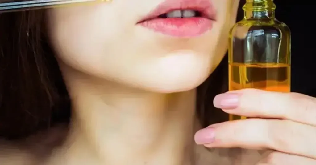 Close-up of a woman applying facial oil using a dropper, holding a bottle of golden-colored oil near her face.